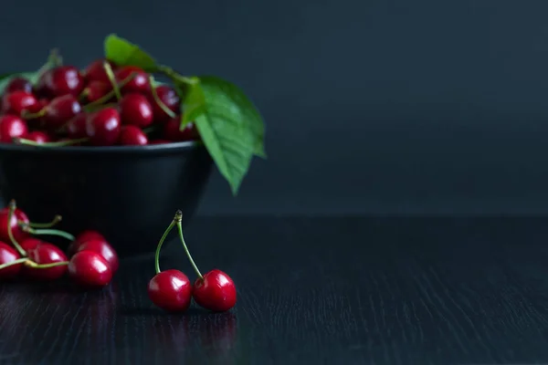 Ciliegia rossa con rametti e foglie primo piano su uno sfondo di un piatto scuro con ciliegie — Foto Stock
