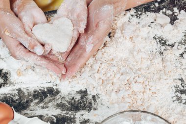 Anne ve kızı hamurdan bir kalp taşıyor. Mutfakta aşçı, siyah bir masanın üstünde yakın plan.