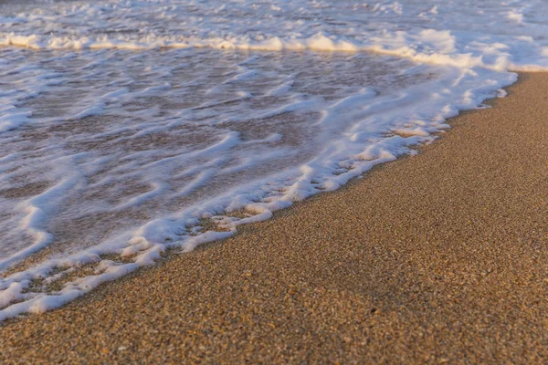 Espuma del agua de mar en la costa de la playa al atardecer —  Fotos de Stock