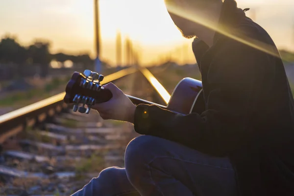 Een jonge kerel zit op de rails en speelt de gitaar — Stockfoto