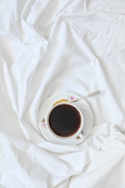 Bir fincan kahve beyaz bir çarşafın üzerinde duruyor.