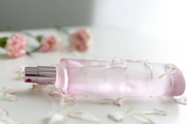 Pembe ve beyaz karanfil çiçek ve yaprakları ile bir pembe parfüm şişesi.