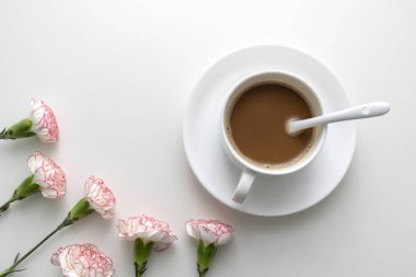 Beyaz masa üzerine pembe ve beyaz karanfil çiçek ile beyaz fincan kahve. Üstten görünüm.