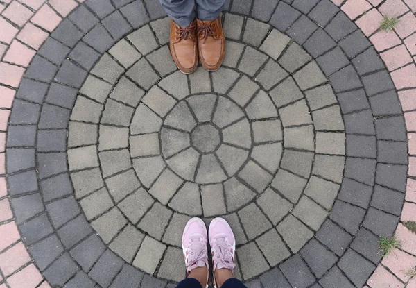 Top view of a couple feet standing on circle shape brick pavement.