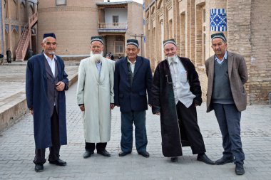 Khiva, Uzbekistan - April 17 2018: Elderly men in traditional Uzbek clothes posing near the mosque in Itchan Kala - historic old town of Khiva clipart