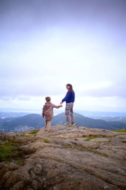 Dağın tepesinde el ele tutuşan iki kız ya da kız kardeş. Bergen, Norveç, 2025. Yüksek kalite fotoğraf