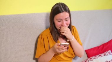 Kız gülüyor, akıllı telefon kullanıyor, utanıyor.