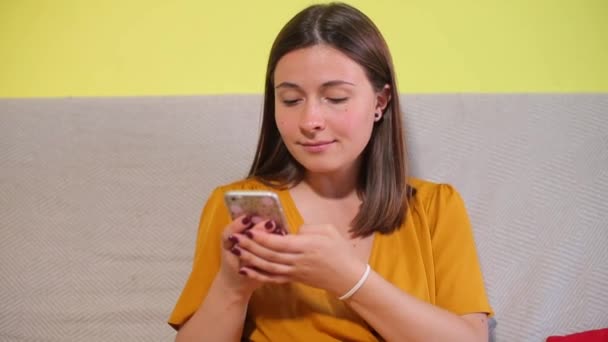 Chica joven utiliza un teléfono inteligente, mira a la cámara — Vídeos de Stock