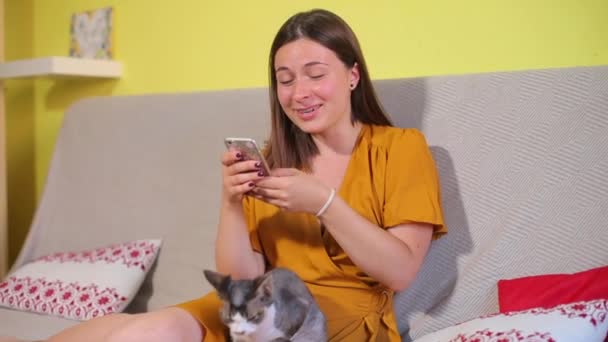 Девушка с котом, используя смартфон, улыбаясь — стоковое видео