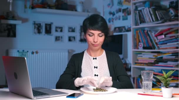 Uma menina sentada em uma mesa em um escritório pega um smartphone e tira fotos de cannabis — Vídeo de Stock