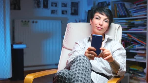 Fille assise sur une chaise utilise un smartphone, en regardant la caméra — Video