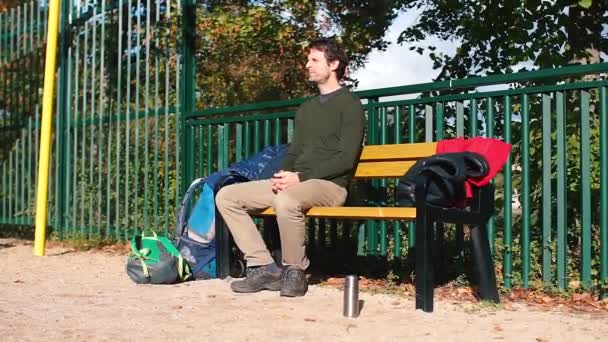 Der Kerl sitzt auf einer Bank im Stadtpark, gähnt. — Stockvideo