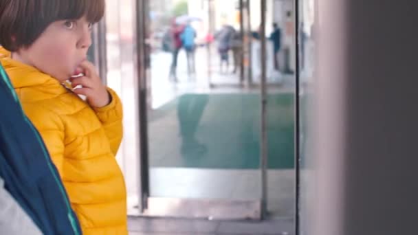 Criança chupa os dedos enquanto está em pé em uma vitrine em uma cidade . — Vídeo de Stock