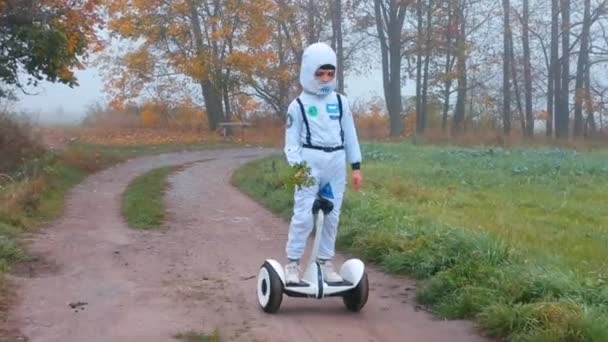 Un niño disfrazado de astronauta monta un giroscooter a través del bosque de otoño . — Vídeos de Stock