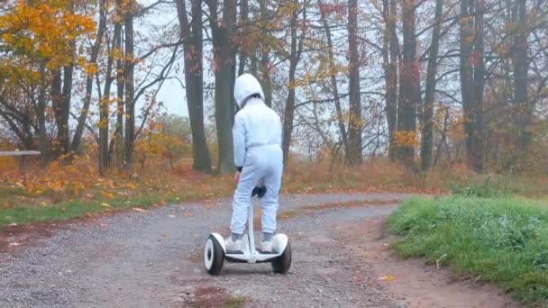 Een jongen in een pak van een astronaut op een gyroscooter maakt een bocht, klimt van hem af. — Stockvideo