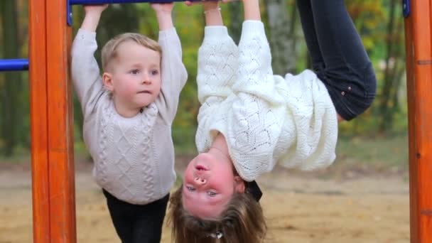 Broer en zus op horizontale tralies. Meisje hangend aan de horizontale balk. — Stockvideo