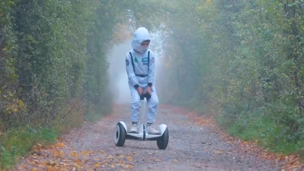 Un niño disfrazado de astronauta monta un giroscooter a través de un bosque nublado — Vídeos de Stock