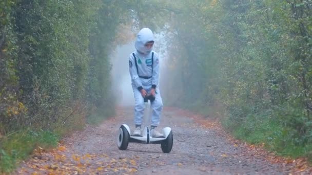 Um rapaz vestido de astronauta monta um giroscópio através de uma floresta nebulosa. — Vídeo de Stock