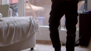A young person engages in a casual morning routine in a cozy, well-lit living space, featuring a sofa and natural light.