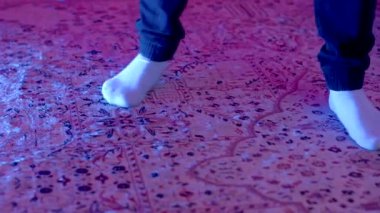 Close-up shots of feet wearing socks dancing on a vibrant, patterned carpet with colorful lighting effects, showcasing movement and joy.