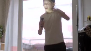 A young boy performs energetically in his living room, using a flashlight as a microphone. His enthusiasm showcases the joy of singing and creativity.