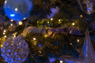 Süslü bir Noel ağacının yakın çekim görüntüsü, renkli süsler ve yanıp sönen ışıklar, neşeli bir atmosfer yaratıyor..