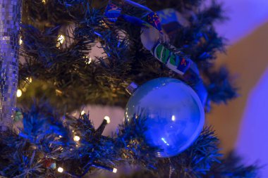 Güzel mavi bir süs, parıldayan ışıklarla çevrili bir Noel ağacını süslüyor, neşeli ve rahat bir atmosfer yaratıyor..