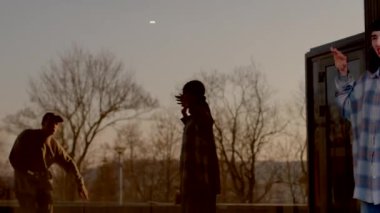 As the sun sets, two men enjoy the view. Friends laugh on the sidewalk. A couple plays frisbee in the park, capturing memories