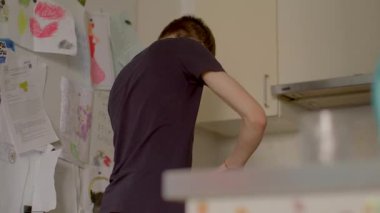 A teenage boy is busy preparing delicious food in a cozy, inviting kitchen, which is adorned with cherished family drawings
