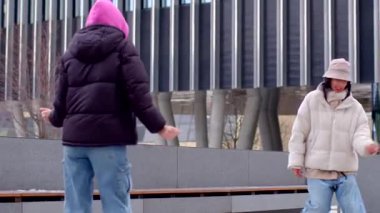 Two women joyfully dance on a park bench by an architectural marvel. A couple joins in, highlighting movement and emotion amid laughter, showcasing community energy