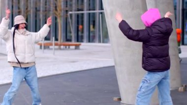 The video depicts an urban scene with two women dancing joyfully on a sidewalk, joined by a little girl and a couple celebrating the moment