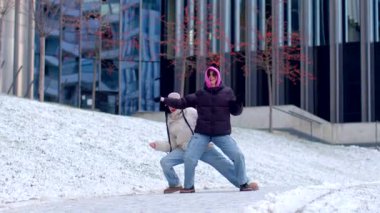 In a winter wonderland, a couple has fun in the snow, dancing joyfully and playfully squatting, embracing love and laughter