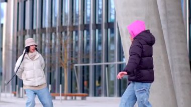 A man and a woman dance joyfully on a lively sidewalk in front of a striking building, captivating onlookers with their energy and love