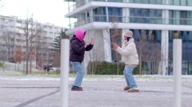 A heartwarming winter video shows a couple dancing in the snow by a charming building. Friends laugh nearby, while young girls celebrate and dance