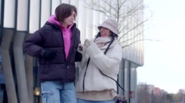 Two young women enjoy a winter day, strolling on a snowcovered sidewalk. They share laughter and warmth, capturing the essence of friendship