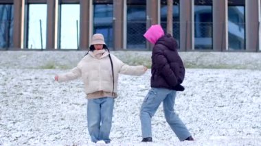 A joyful winter scene of a couple dancing and playing in the snow in front of a picturesque building, having fun with snowball fights