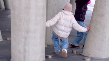 In an urban scene, a man relaxes on a pillar while groups mingle. A woman in a pink hoodie connects with a man, showing city friendship