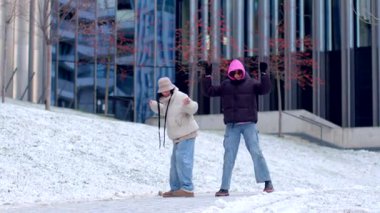 In a winter setting, a man and woman joyfully dance in the snow by a charming building, capturing a magical day filled with laughter