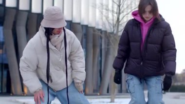 A man and woman stroll hand in hand through a snowy street, joined by two women. They dance joyfully in the serene winter landscape