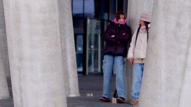 A man and woman share quality time in an urban setting, standing close on a sidewalk, leaning against a column, enjoying each others company