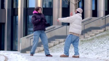 In a winter setting, a man proposes to a woman in the snow, creating a warm, joyful scene. Two women dance playfully, enhancing the atmosphere