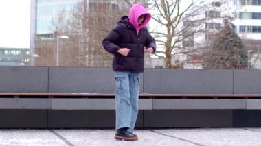 A man in a pink hoodie and black jacket talks casually with a woman by a bench in an urban setting, showcasing camaraderie and connection