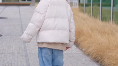 This video shows a woman in a white jacket and blue jeans walking down a busy sidewalk, pausing to enjoy her surroundings with confidence