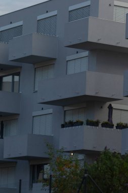 Contemporary architecture featuring a multi-story apartment building with sleek balconies and lush green plants below.