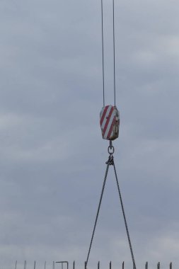 A detailed view of an industrial crane pulley set against a dramatic cloudy sky, showcasing construction and engineering elements.