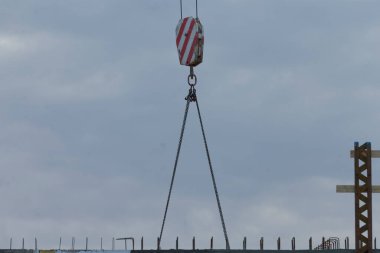 A crane hook suspended in mid-air at a construction site, set against a backdrop of cloudy skies, showcasing the industrial environment.