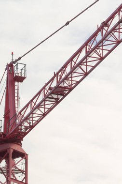 Gökyüzü bulutlu, sanayi mühendisliği ve kentsel gelişimi gösteren yüksek kırmızı bir vinç zemin üzerinde beliriyor..