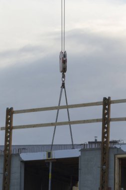 A construction crane with a pulley system is seen lifting materials at a building site, showcasing heavy machinery in action under a cloudy sky.