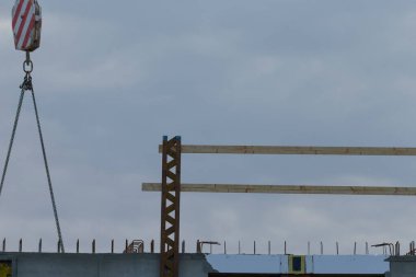 A construction site featuring a crane lifting wooden beams against a cloudy sky. The scene captures the essence of modern building projects.