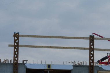 A construction site featuring wooden beams under a cloudy sky, showcasing the framework of a building in progress with construction equipment visible.